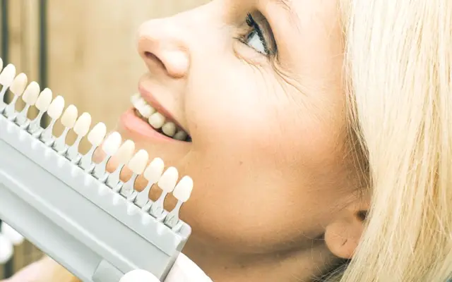 Smiling patient as the dentist matches her tooth shade for veneers